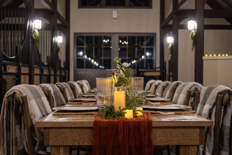 Long banquet table set with candles and a rust runner in a barn aisle at night