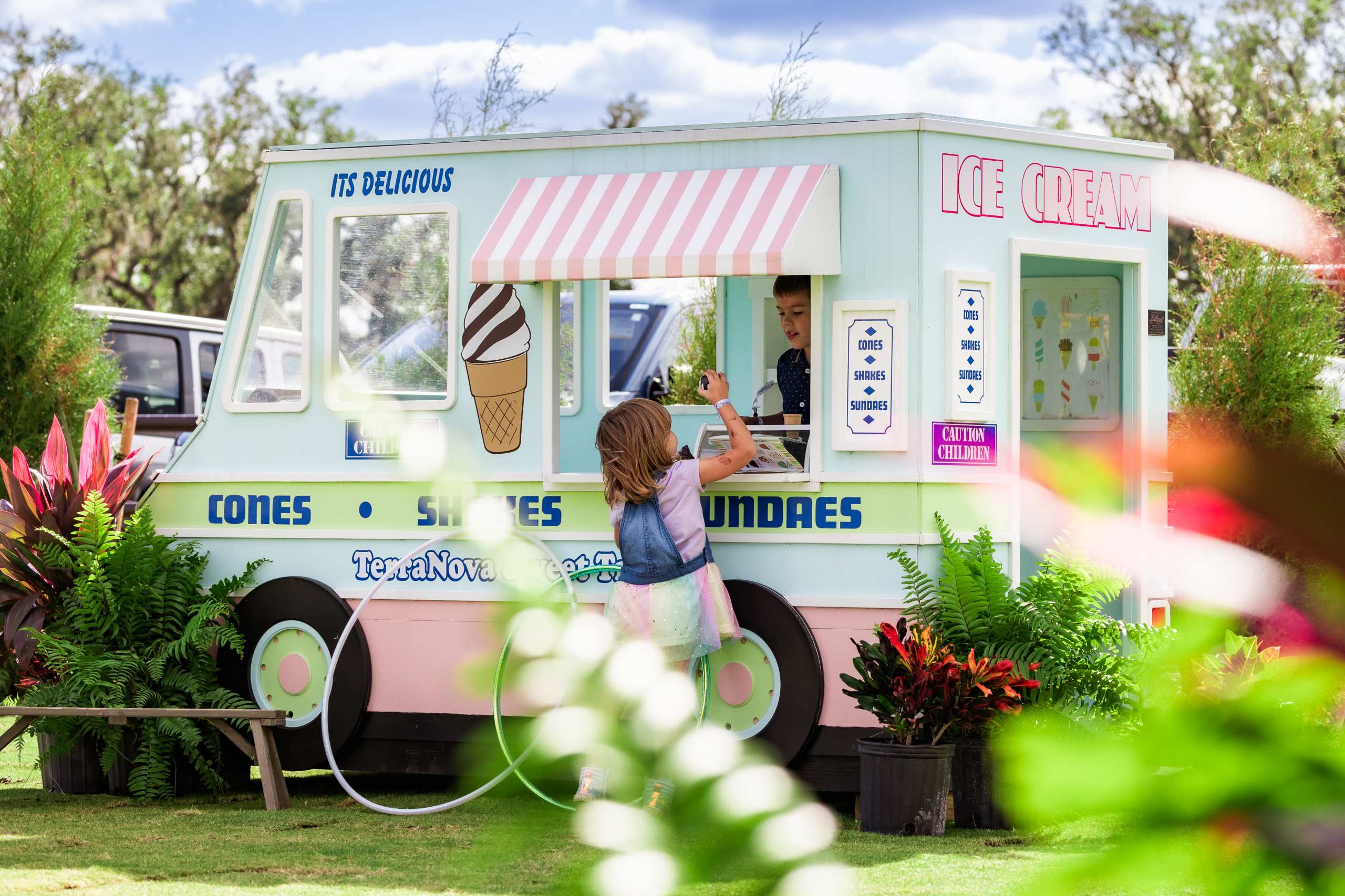 Child reaches up to the window of a pastel ice cream truck on the lawn