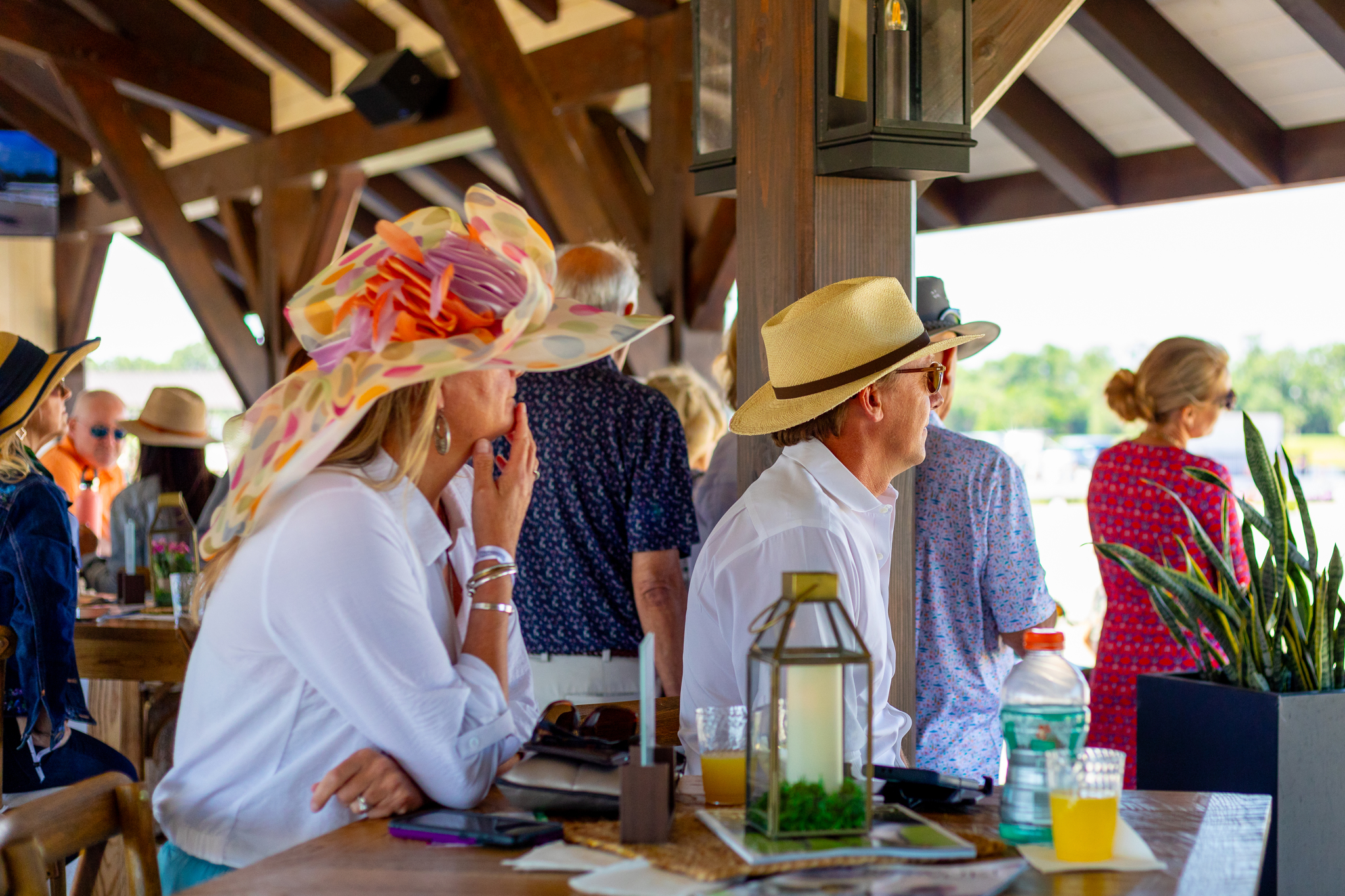 Guests in sun hats sit along the bar rail under the timber pavilion roof