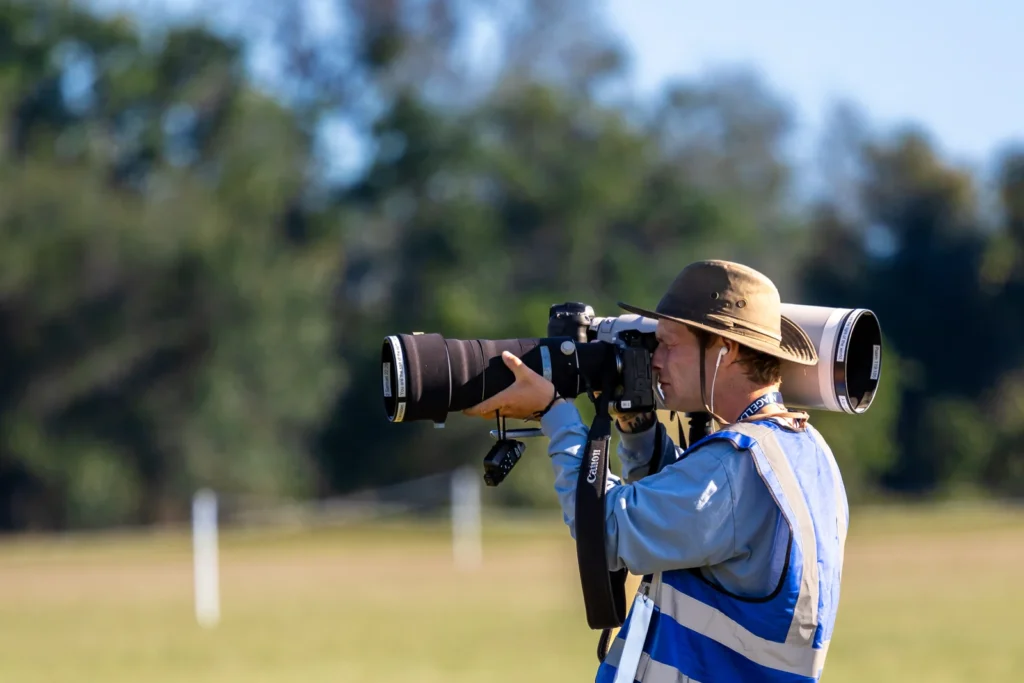 Photographer in a blue tabard and bush hat shoots with a long telephoto lens