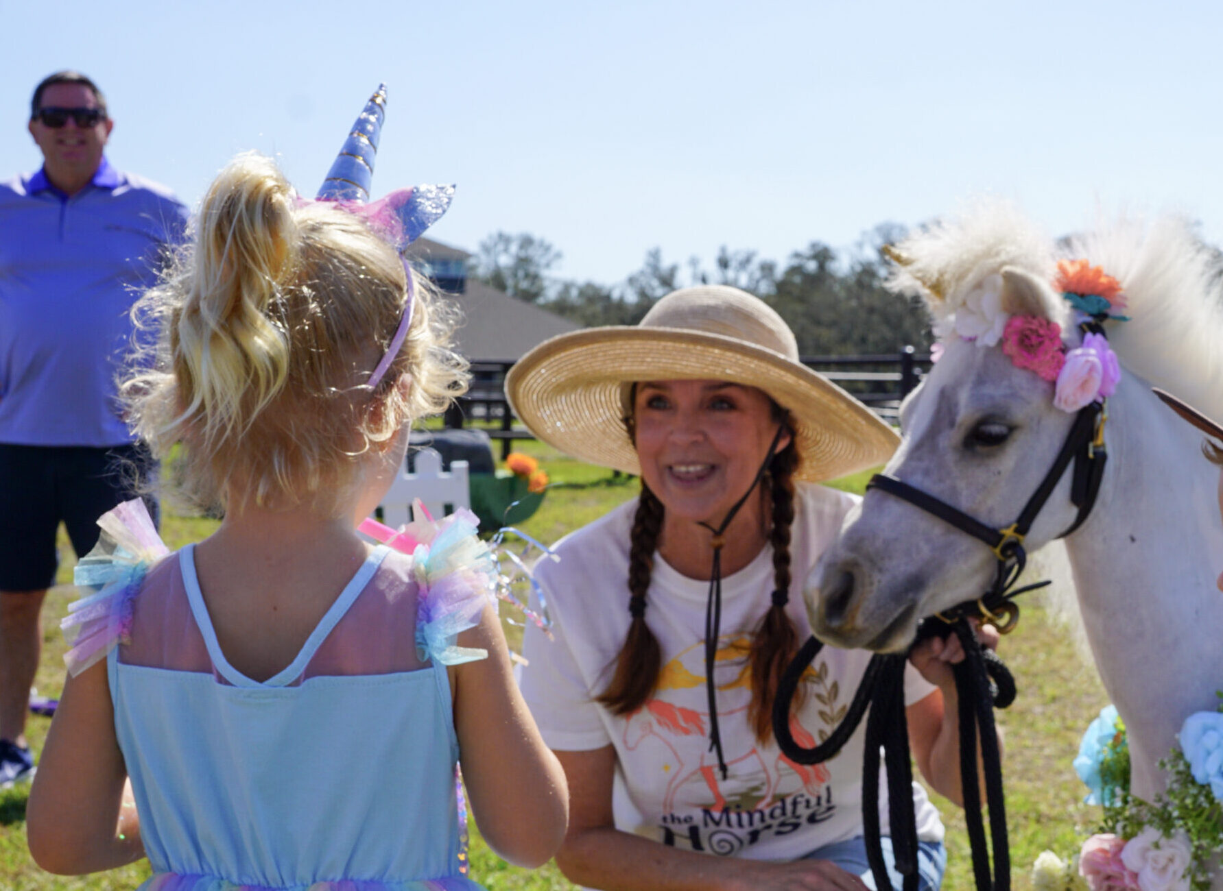 Girl in a unicorn costume meets a white miniature horse in a flower crown