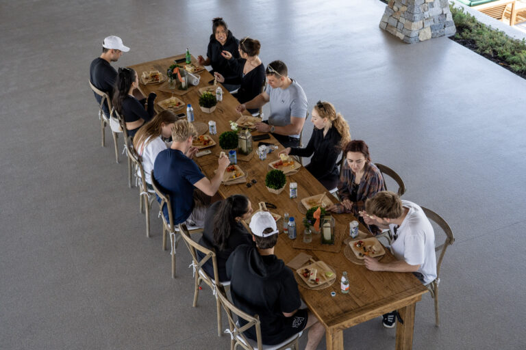 Overhead view of a group eating together at a long wooden table on a covered patio