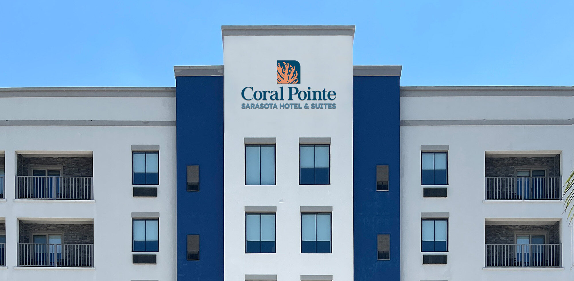 White and navy hotel facade with the Coral Pointe Sarasota Hotel and Suites sign
