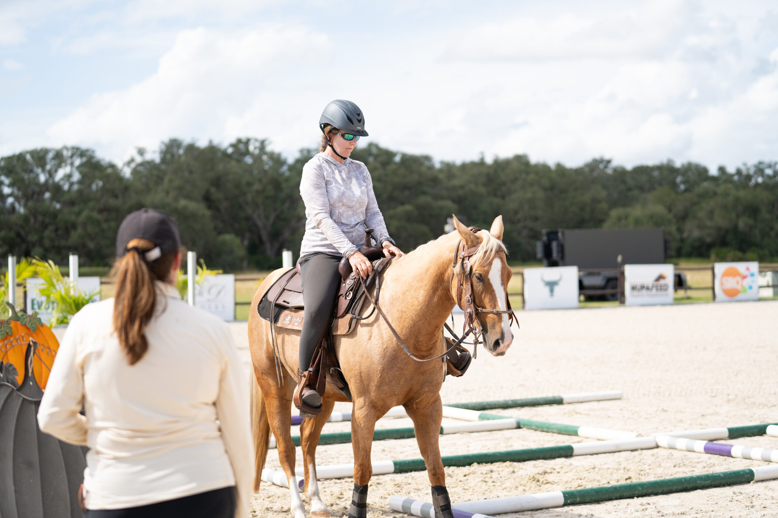 Rider sits on a palomino horse in a western saddle beside a trainer in the arena