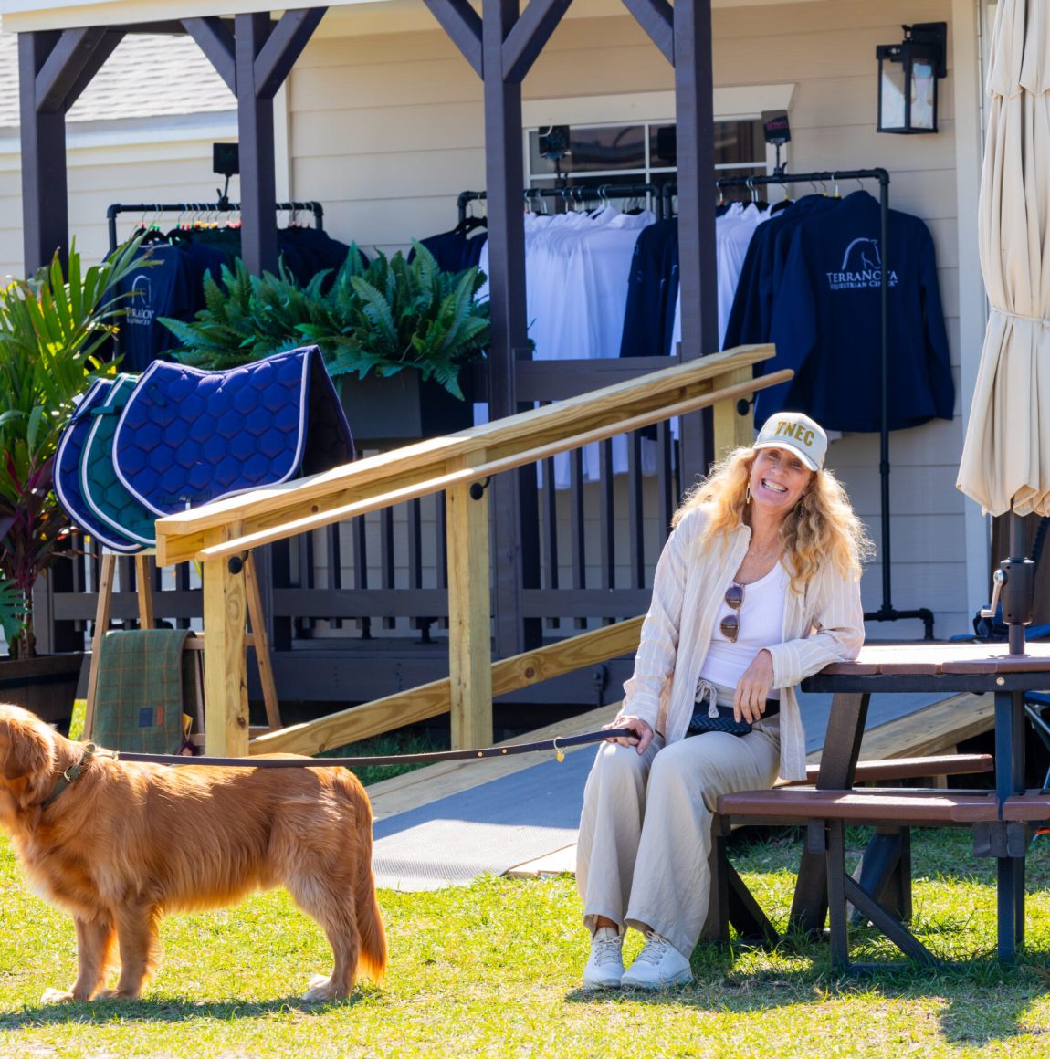 Woman sits at a picnic table outside a boutique cottage with a golden retriever nearby